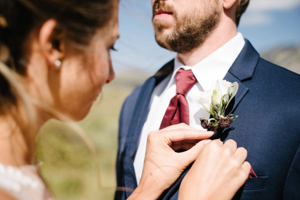 bride pinning the boutonniere on the lapel of the groom