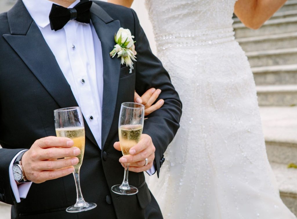 Groom in his tux with champagne and the bride - Jim's Formal Wear