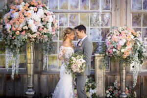 bride and groom sharing an embrace in front of a large display of flowers and stained glass windows
