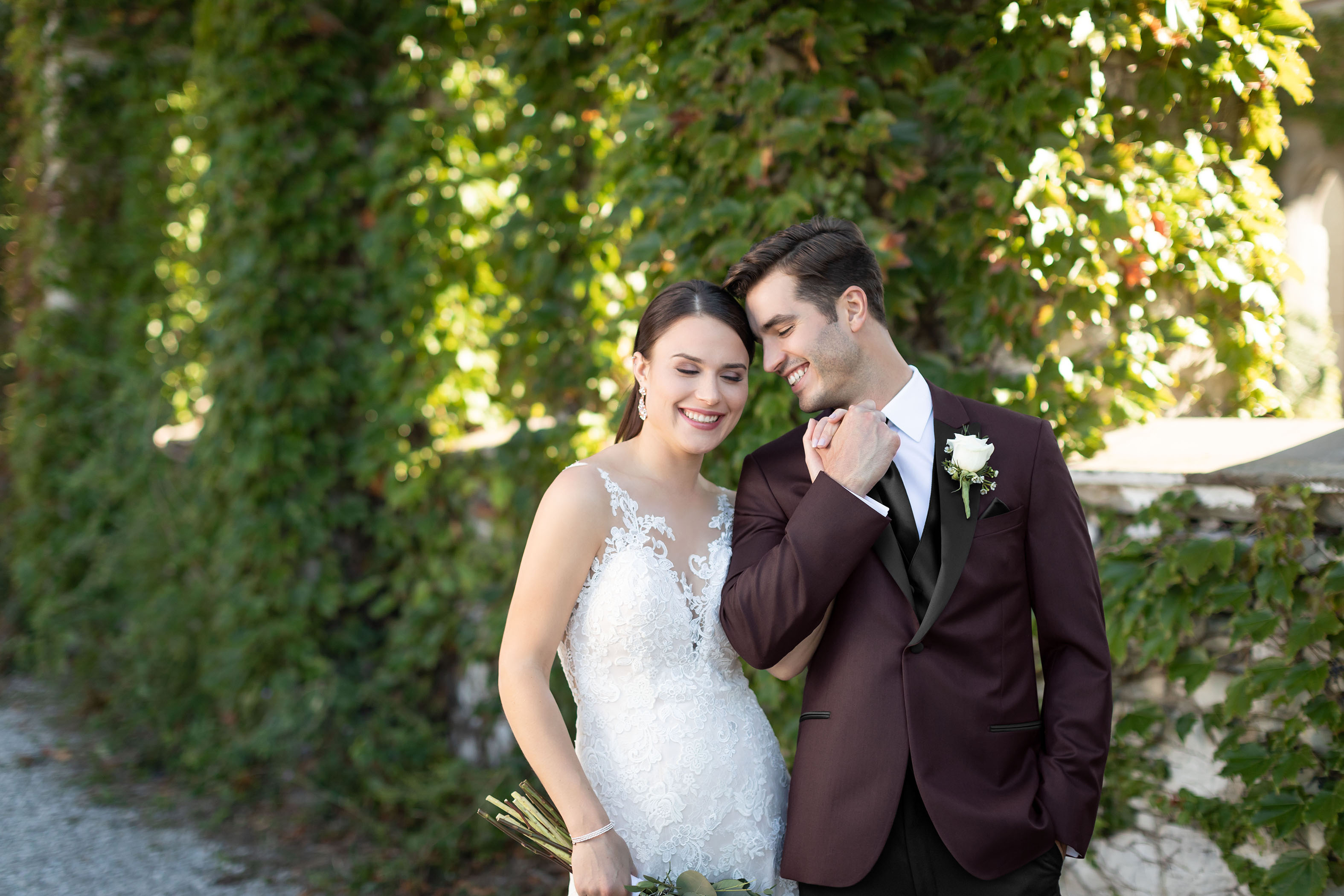 Bride and Groom smiling in front of vines , Groom is wearing a Custom Tuxedo