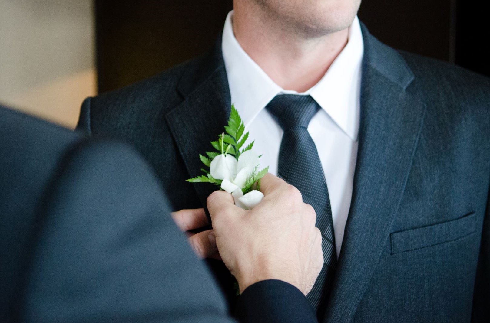 How to wear a boutonniere - Friend helping attach a boutonniere to a suit