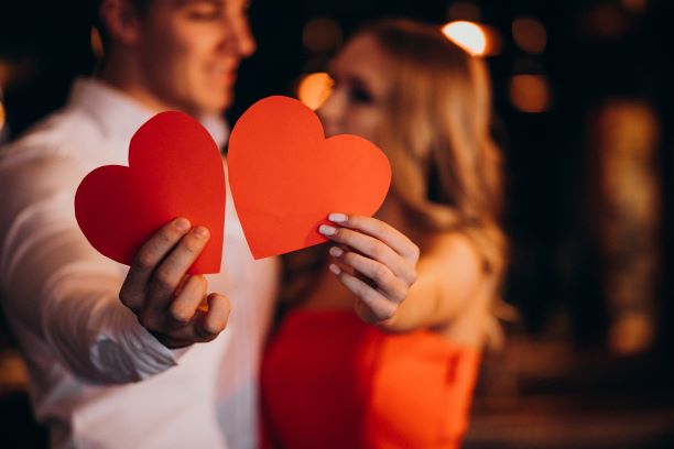 valentine's day man and woman holding two red paper hearts