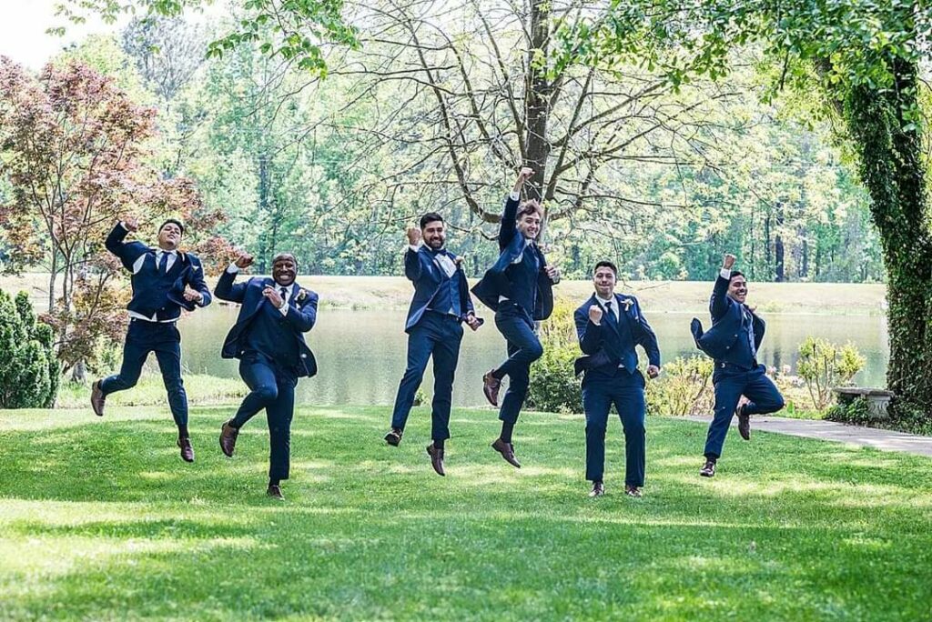 groom and groomsmen in blue suits jumping for joy