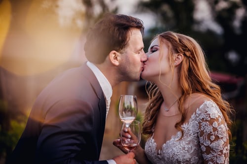 bride and groom kissing with glass of wine