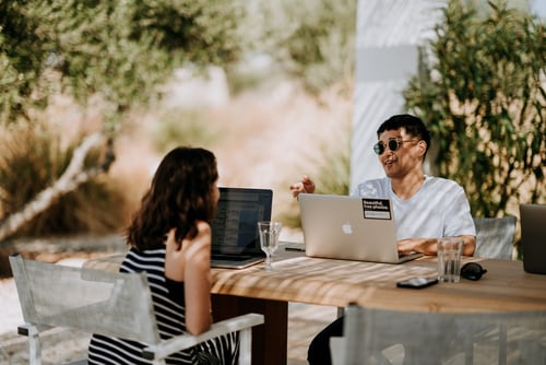 man and women sitting outside at table with laptops setting a wedding date