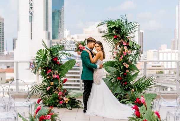 groom in green jacket with bride infront of tropical flowers