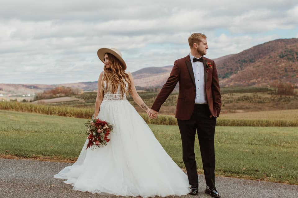 bride in bridal gown with hat and groom in burgundy tux jacket