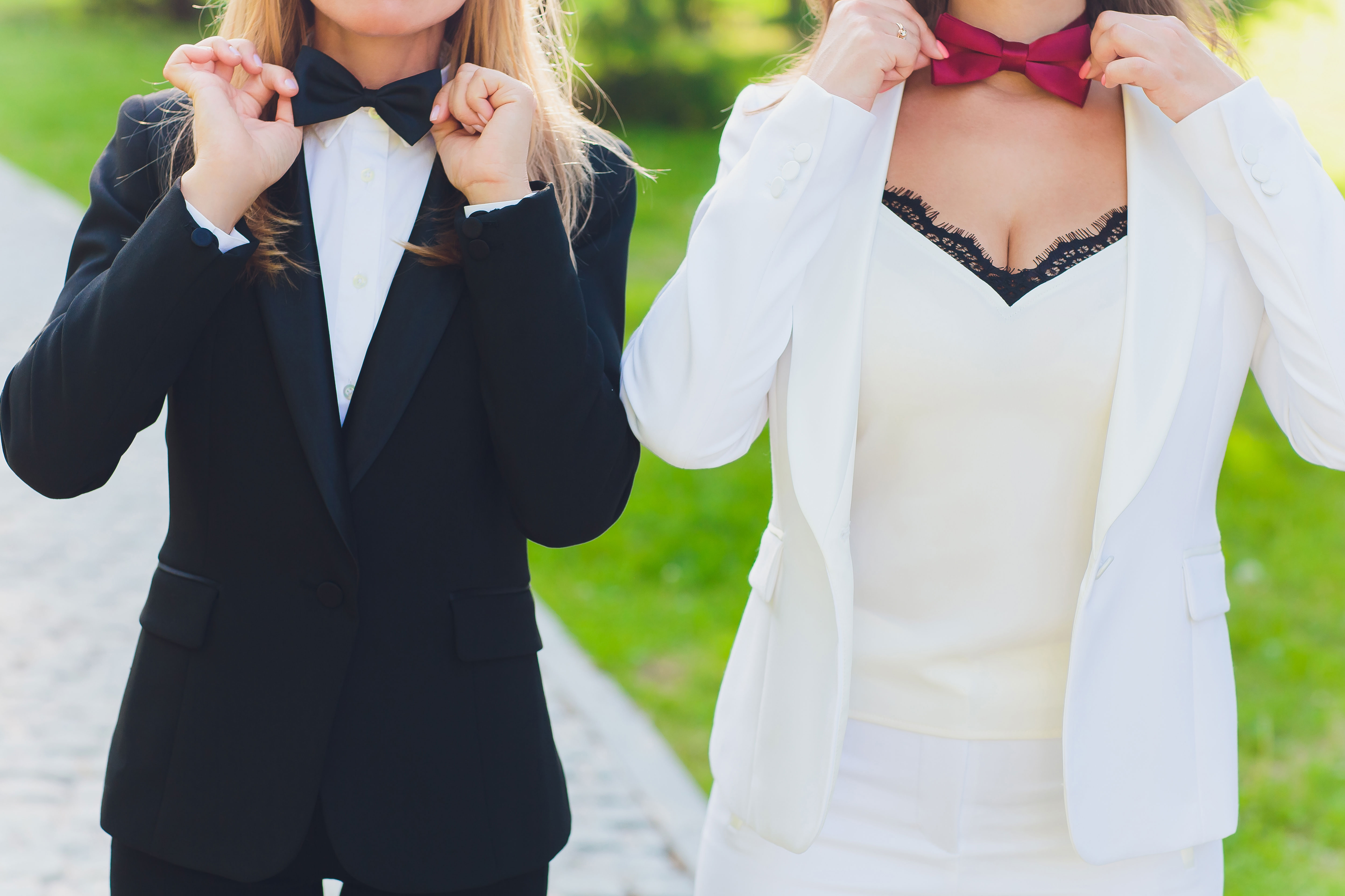 one woman in black tux with black bow tie and another woman in white tux with red bow tie