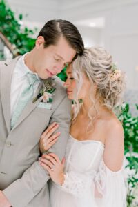 groom in sand colored wedding suit with floral sage green tie standing next to bride in wedding dress