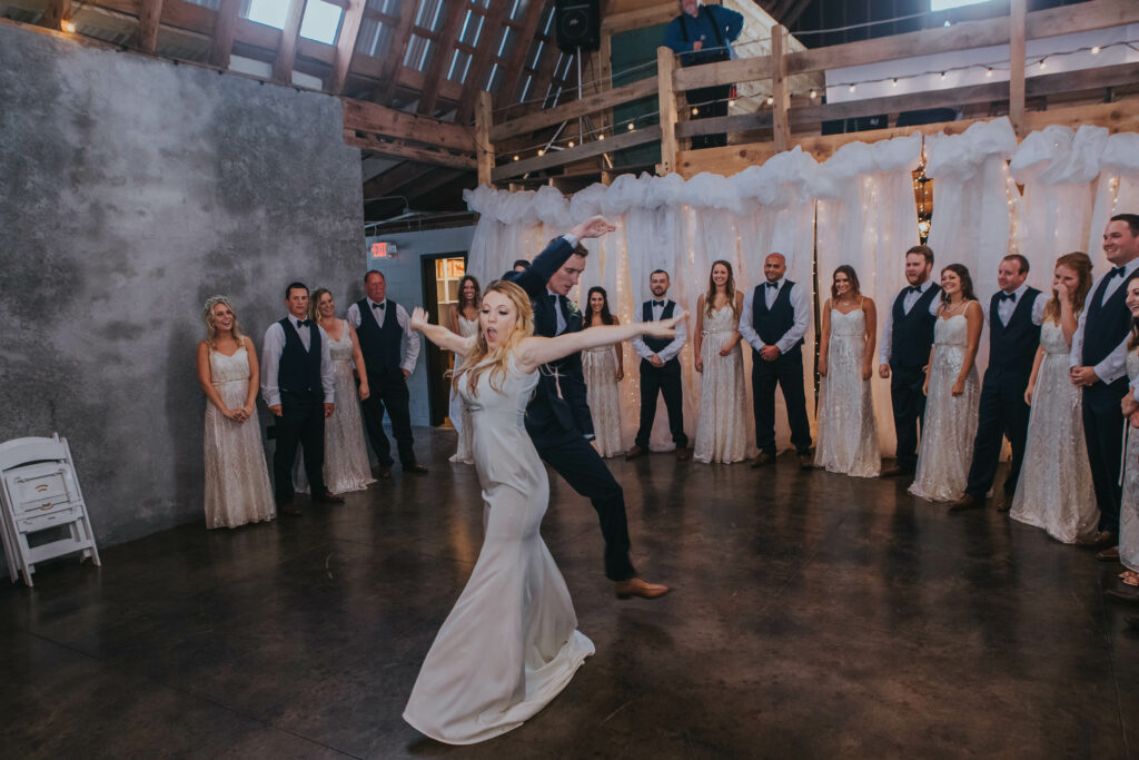 bride in silk dress and groom in navy suit dance together as bridal party circle around them