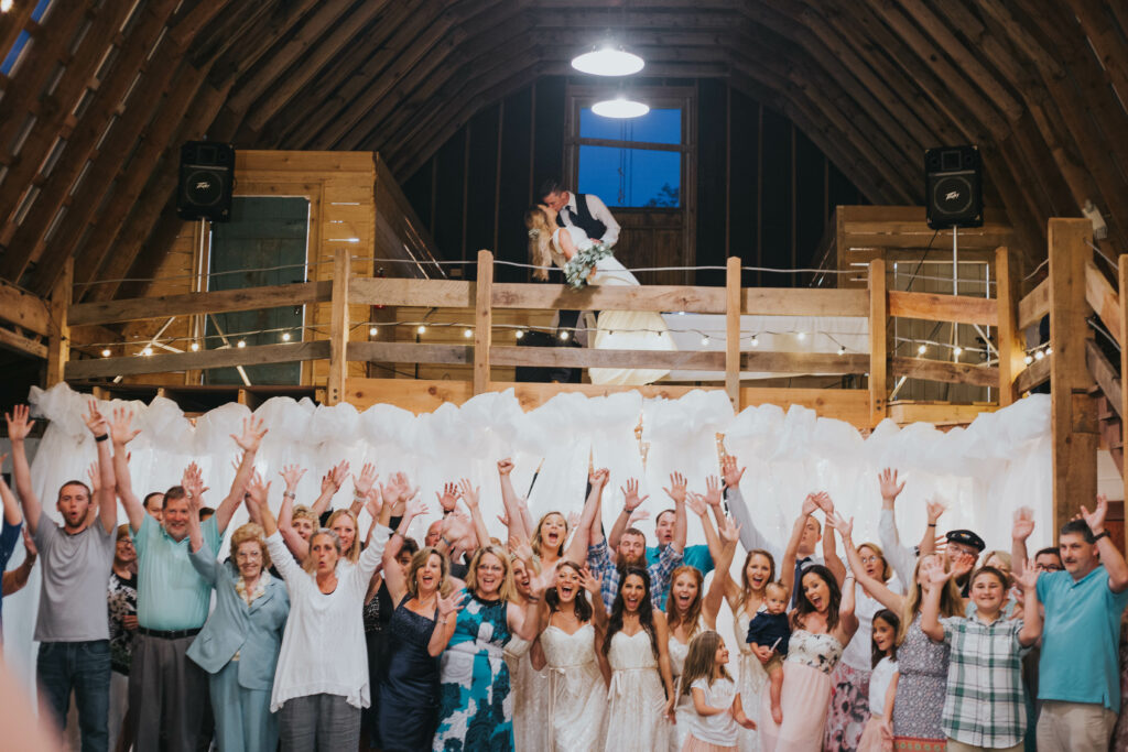 anniversary reception- bride and groom embraced in a kiss on a balcony as all the wedding guests stand below smiling for the camera