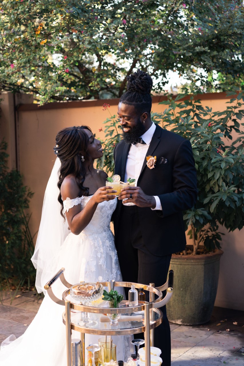 Bride and groom holding drinks in front of bar cart. Trending Wedding Bar Ideas.