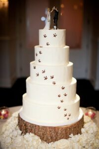 wedding cake with paw prints going up, wedding cake toppe of bride and groom high fiving, dog sitting next to them