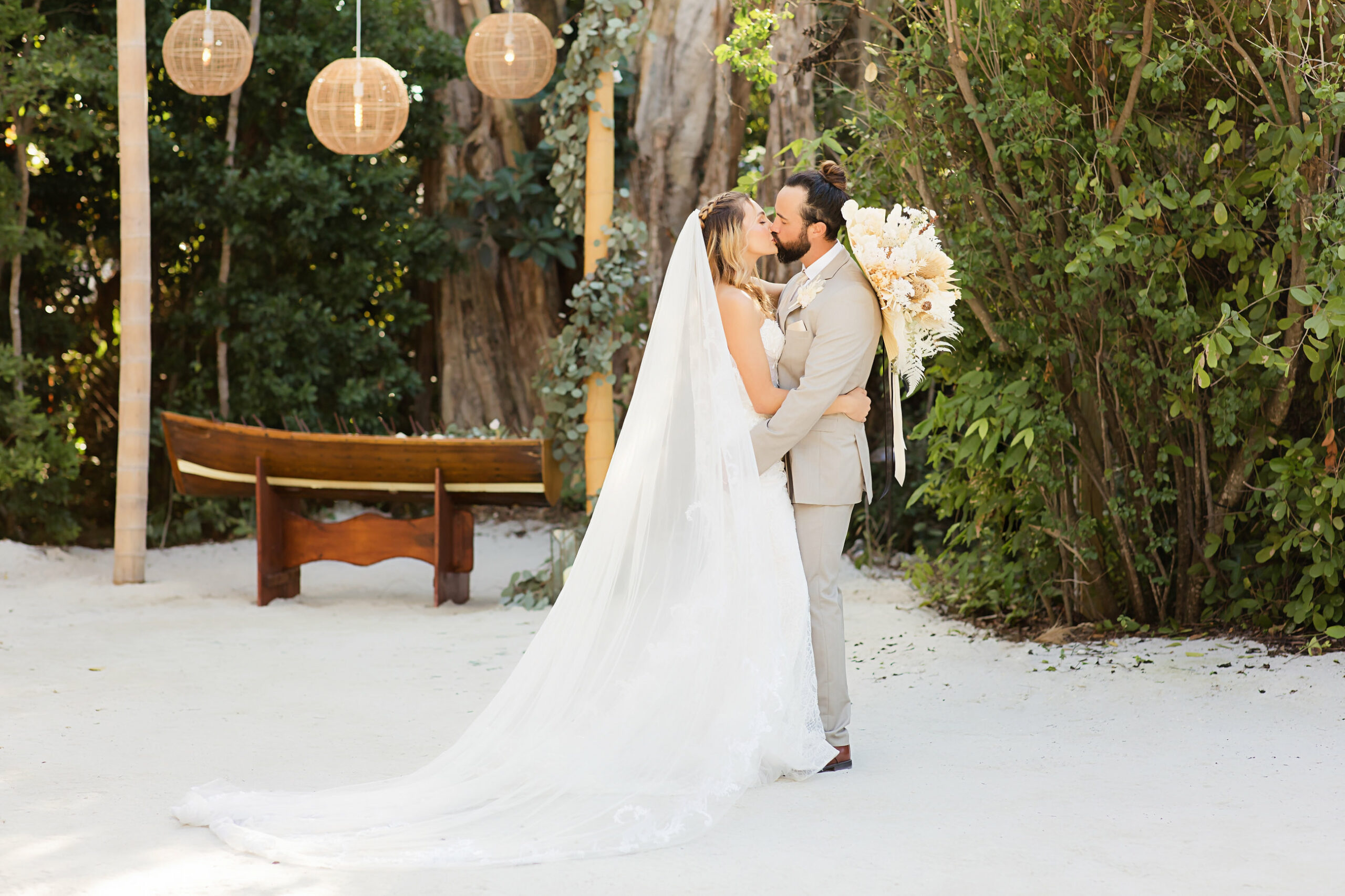 bride in white dress and groom in tan suit kissing on beach