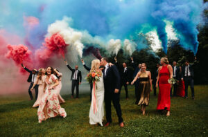 Wedding party walking through grass holding red, white and blue smoke bombs. Festive Americana Wedding Must Haves