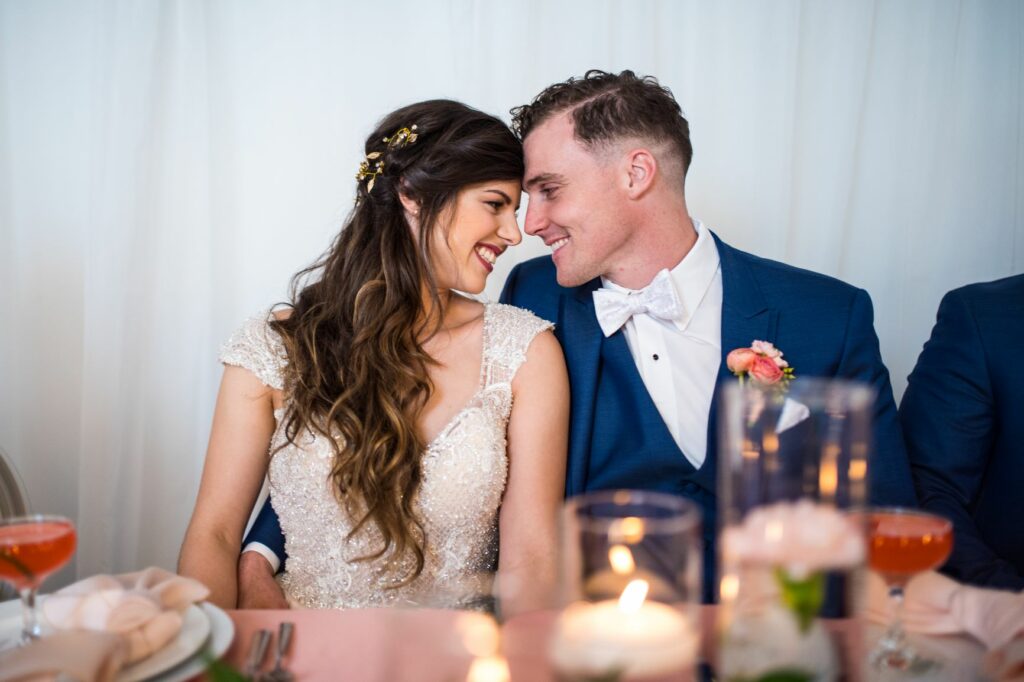 bride and groom wearing a custom tuxedo sitting close together at their head table