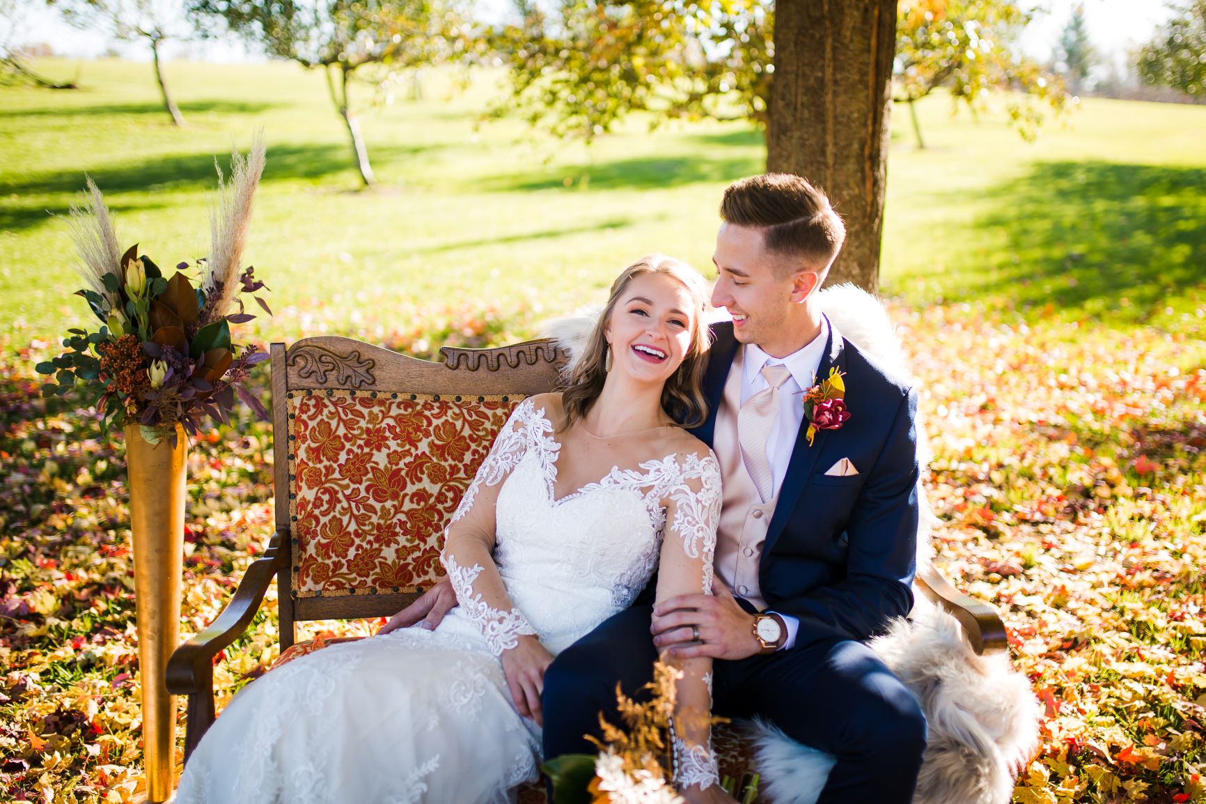 bride and groom sitting on a couch in a grassy area surrounded by fall foliage