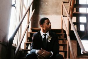 black guy in a rental suit in black sitting on the stairs