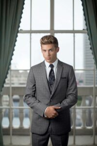 guy in grey plaid suit standing infront of window 