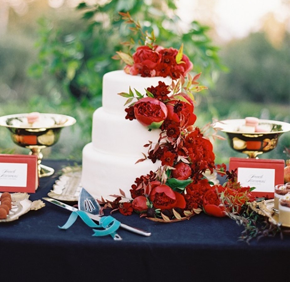 wedding cake with red flowers cascading down the side on a navy blue tablecloth