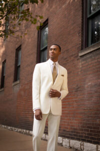guy walking down the street in ivory tuxedo with gold tie, vest and pocket square