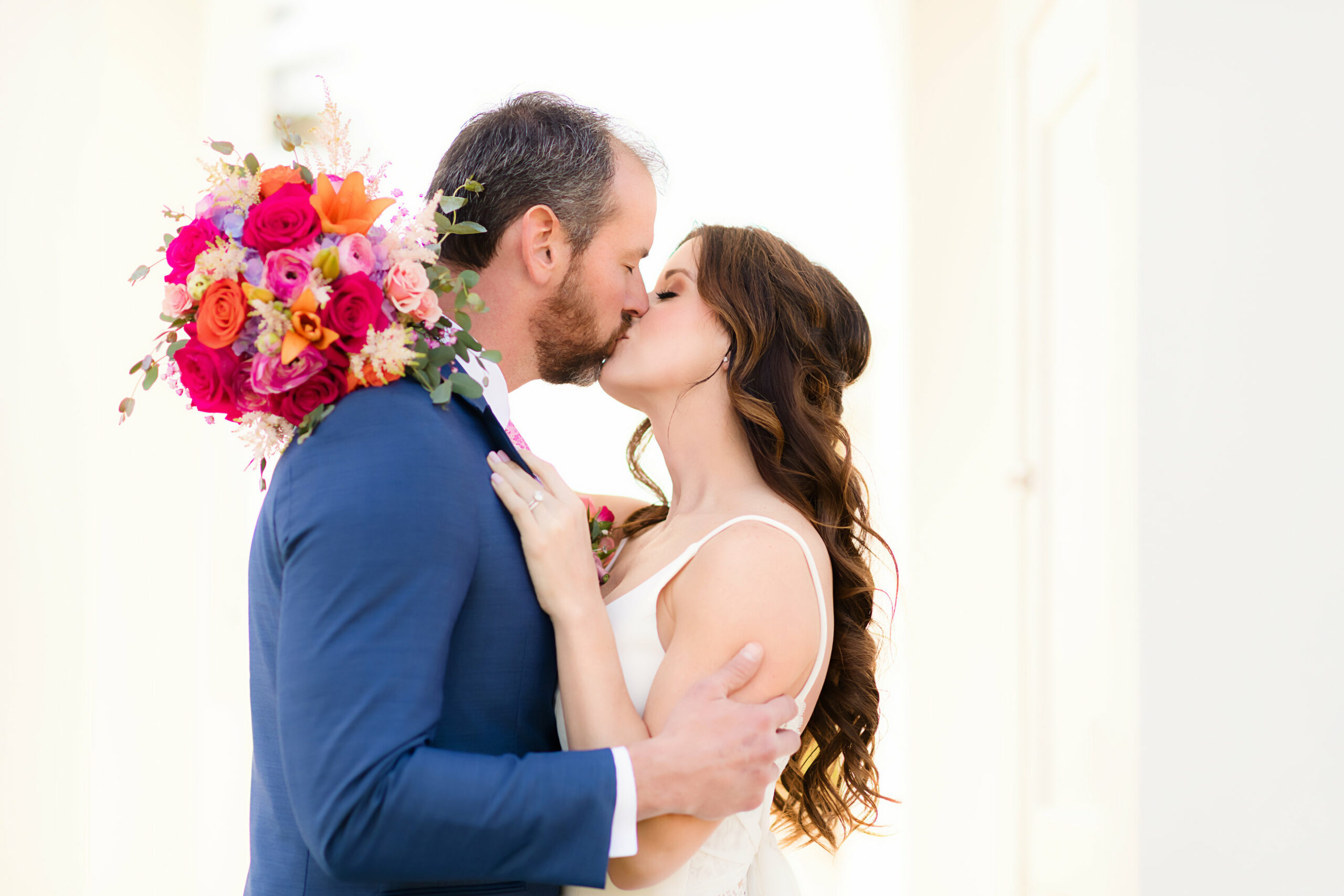 Bride and groom kissing, bride holding brightly colored wedding flowers