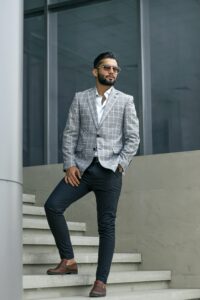 man standing on stairs wearing casual wedding attire including a light grey plaid sport coat and dark pants