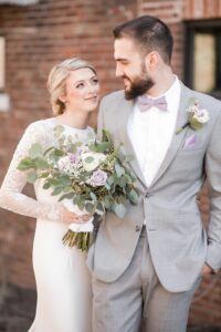 bride and groom looking at each other, bride hold bouquet of lavender and white roses