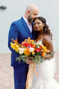 groom kissing top of bride's head while she is looking foward, holding a bouquet of poppies and assorted wedding flowers