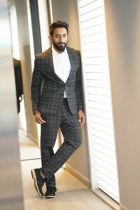 man wearing grey plaid suit and no tie while leaning again wall 