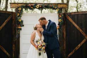 Bride and groom kissing, bride holding bouquet of sunflowers and roses