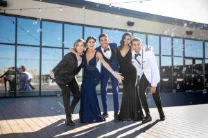 3 high school boys in tuxes and 2 high school girls in prom dresses posing in front of building