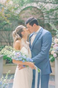 bride and groom kissing. Bride is in white, sleeveless wedding dress, groom in light blue suit