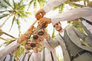 best man do's - group of guys at a bachelor party in a tropical area, toasting with beers