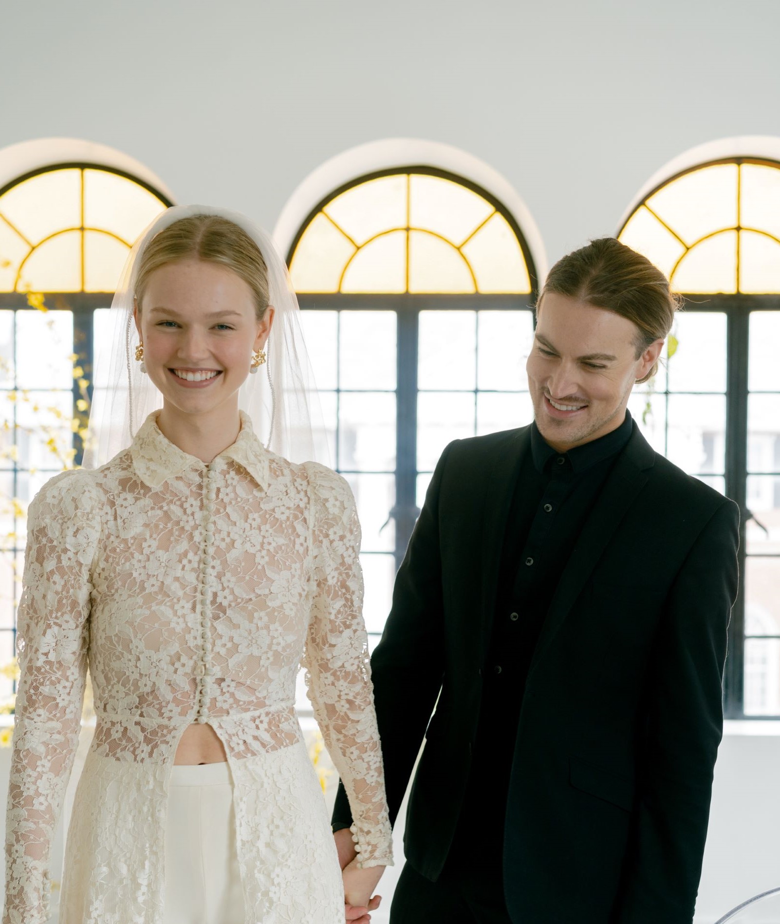 bride wearing ivory dress pants and lace ivory top and groom in all black tux