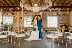 bride in white wedding dress, groom is a female in a cobalt blue tuxedo with black lapels. she is looking at the bride and has arms around waist