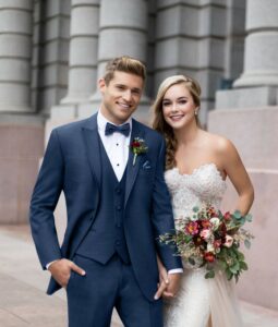 bride and groom standing next to each other, groom in blue tuxedo with matching bowtie and vest