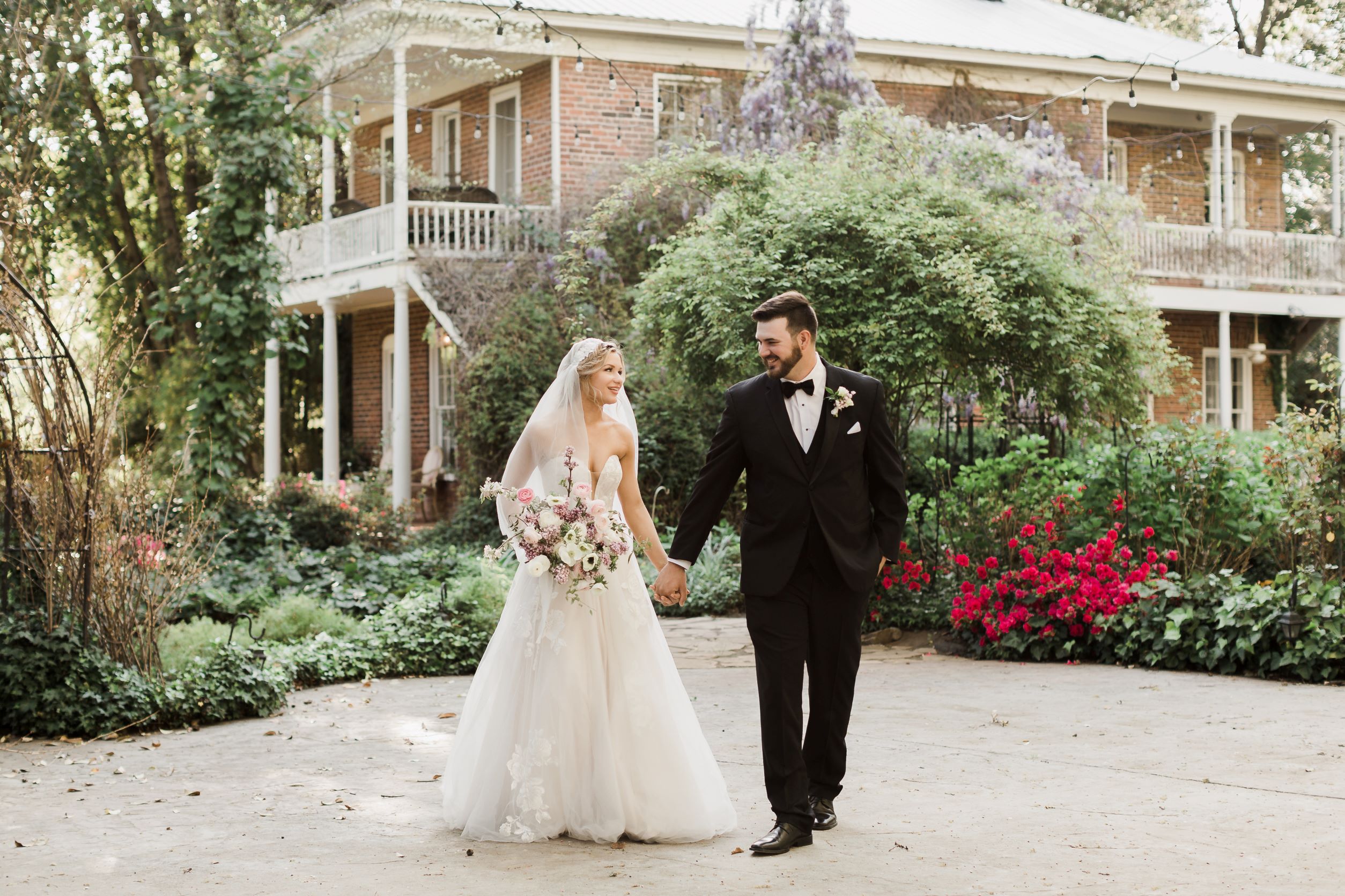 bride and groom holding hands, walking and looking at each other. Bride in white dress, groom in black tuxedo