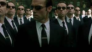 Agent Smith from the Matrix movies and his clones. Guy wearing sunglasses, black suit, black long tie with silver tie clip