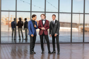 three high school boys wearing paisley jackets. One in blue, one in red, one in granite. Standing in front of large window.