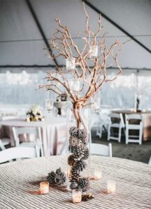 table centerpiece of bare branches in tall vase that has pinecones inside. candles hanging from branches and around vase.