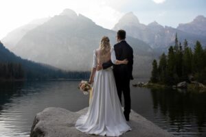 bride and groom standing next to each other with their backs to the camera, looking at a Montain at Jackson Hole, WY