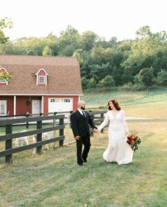 bride and groom holding hands, walking. Family farm behind them