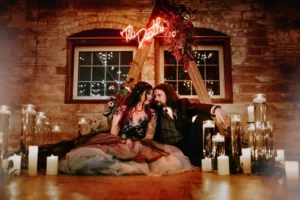 bride and groom sitting on floor, surrounded by candles, neon sign reads 'Til Death for a Friday the 13th inspired 2024 wedding date