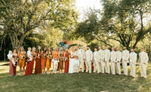 wedding party line up. Bridesmaids in different dresses, different shades of orange. Groomsmen in tan suits
