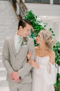 groom in tan suit, sage floral tie. Looking at bride. Bride looking at groom, hand on his arm