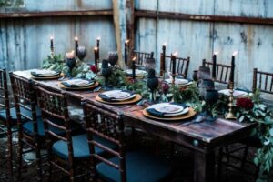 table setting for a moody wedding, greenery runner down the middle with gold plates, tall black candles down the center.