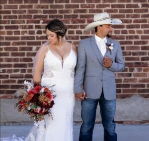 Bride holding a large bouquet and groom wearing jeans, grey suit coat and western cowboy hat
