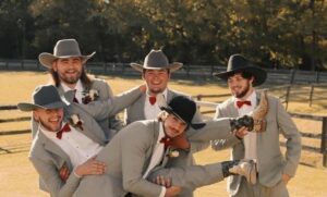 group of 5 men wearing tuxedos and western cowboy hats in a pasture