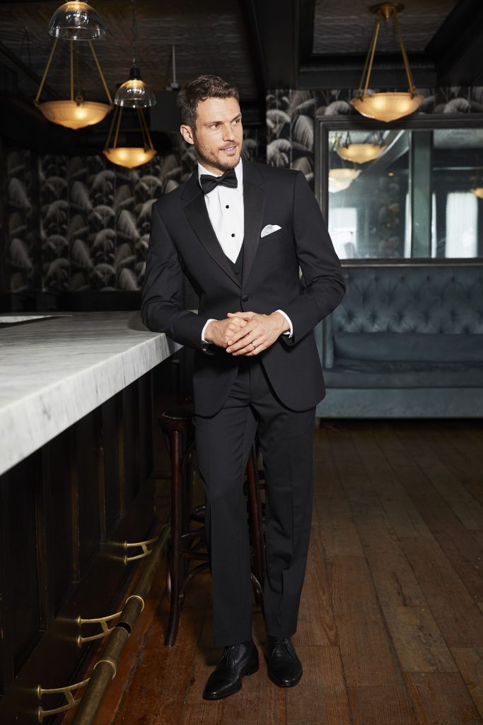 Man in a tuxedo leaning on a bar